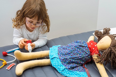 A little girl giving a shot to her doll.