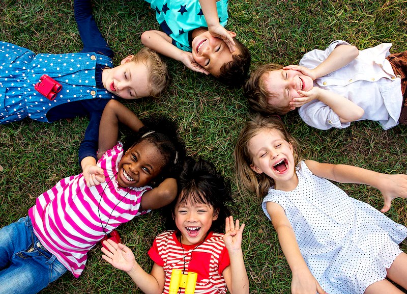 Six smiling and laughing children laying on the grass in a circle.