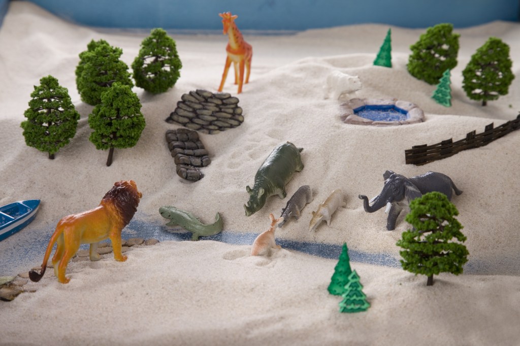 Toy forest scene with zoo animals in the sand.